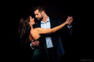 Close up back rear behind photo beautiful she her wife he him his husband mrs mr married spouse hold hands tango slow dance position gentle wear costume jacket green dress isolated black background